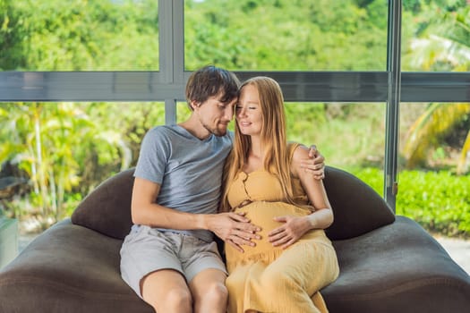 A tender moment captured as a husband and pregnant wife sit on the sofa, sharing an affectionate hug, their love and anticipation radiating in their embrace.