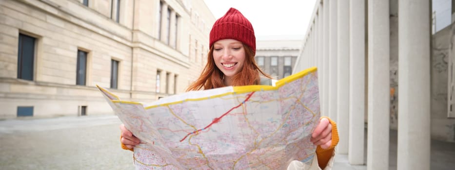 Redhead girl, tourist explores city, looks at paper map to find way for historical landmarks, woman on her trip around euope searches for sightseeing.