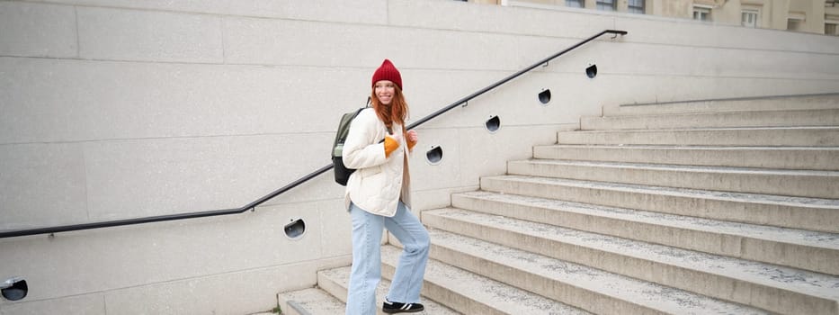 Young stylish girl traveller goes sightseeing, travels around city with backpack, tourist smiles and looks around. Copy space