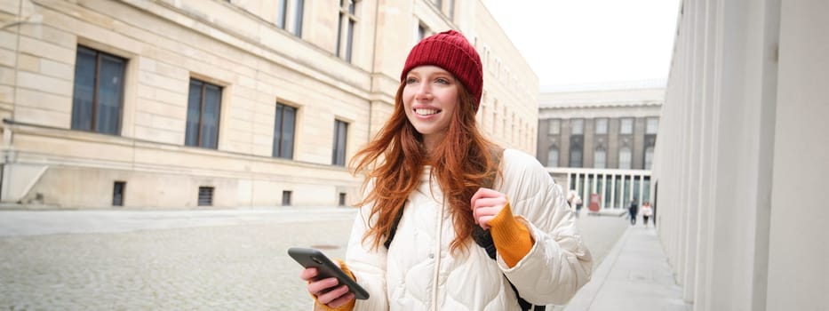 Tourism and technology. Beautiful redhead girl tourist, looking for a route on application, using city map on smartphone, reading about sightseeing places on mobile phone.