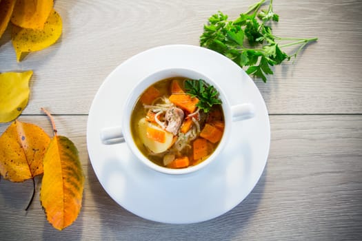 Autumn soup with chicken, noodles and autumn vegetables in a bowl on a wooden table.