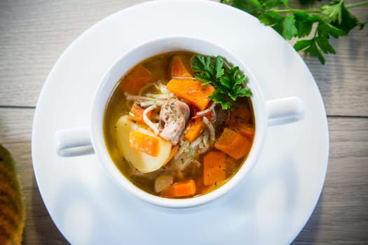 Autumn soup with chicken, noodles and autumn vegetables in a bowl on a wooden table.