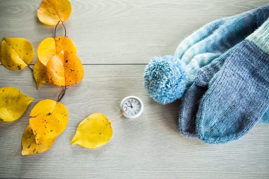 Autumn foliage, winter mittens and a clock on a wooden table. Change to winter time.