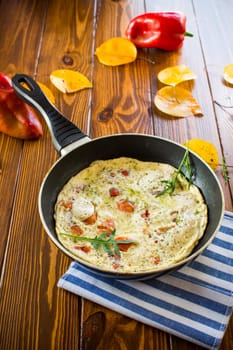 Fried omelets with various autumn vegetables in a frying pan on a wooden table. Autumn recipes.