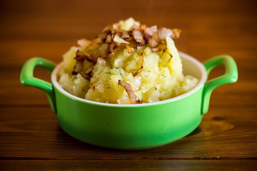 Cooked mashed potatoes with fried chopped bacon and onions in a bowl.