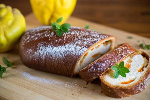 Cooked sweet pie with quince and pumpkin inside, yeast dough roll, on a wooden table.