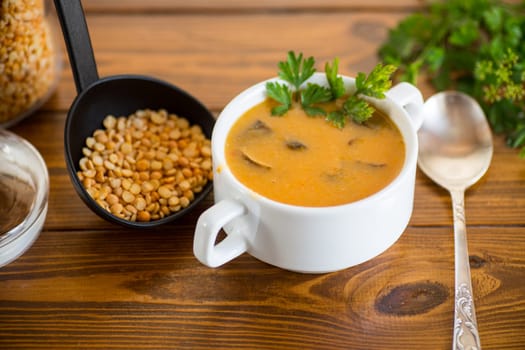 Cooked dried pea puree soup with mushrooms in a bowl on a dark wooden table.