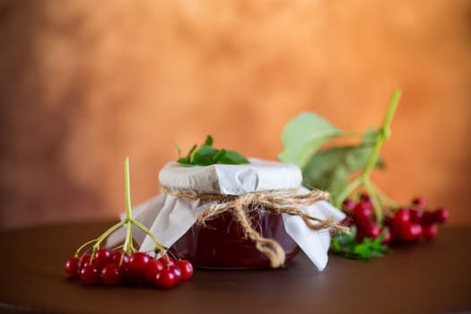 viburnum jam in a glass jar and fresh red viburnum on a light wooden table.