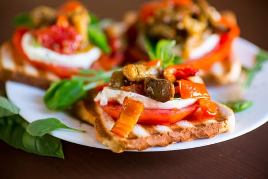 Prepared sandwich with tomatoes, mozzarella and fried eggplant with mushrooms in a plate on a wooden table.
