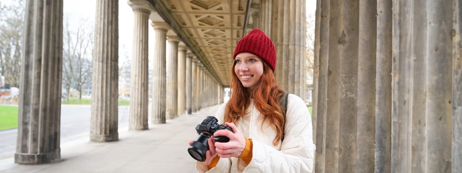 Smiling tourist photographer, takes picture during her trip, holds professional camera and makes photos. Copy space