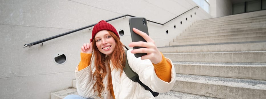 Urban girl takes selfie on street stairs, uses smartphone app to take photo of herself, poses for social media application.