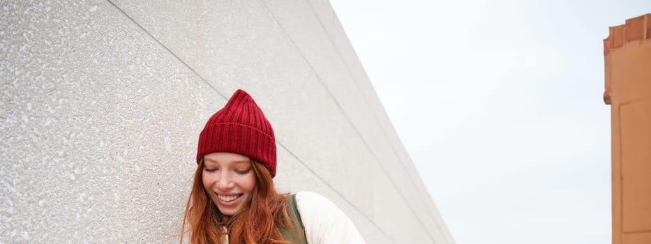 Joyful girl tourist looks at mobile phone, texts message on smartphone social media application, walks around city, looks for sightseeing on mobile app.