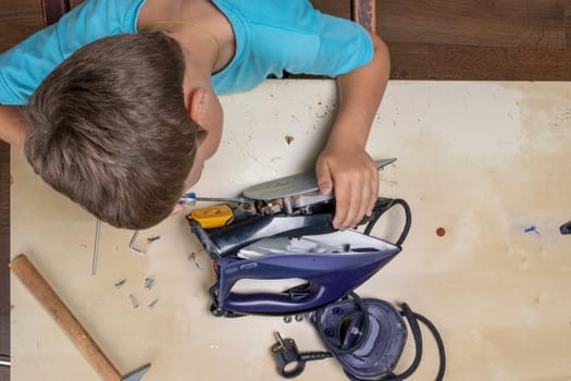 boy helps his mother. a funny master repairs an electric iron on the table using tools. Disassembled electric iron.