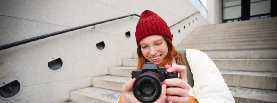 Urban people and lifestyle. Happy redhead woman takes photos, holding professional digital camera, photographing on streets.