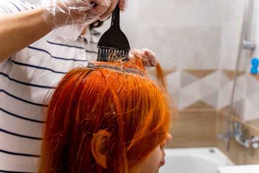 Profile of a pretty teenage girl coloring her hair red. The process of dyeing hair red. Style and modern fashion