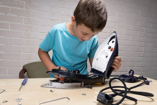 boy helps his mother. a funny master repairs an electric iron on the table using tools. Disassembled electric iron.
