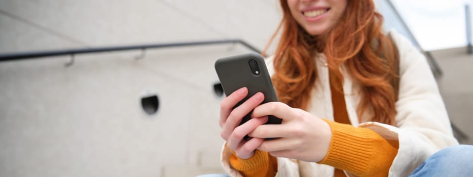 Close up portrait of girls hands holding smartphone. Woman sits on stairs on street and uses mobile phone, chats, reads message or uses application.