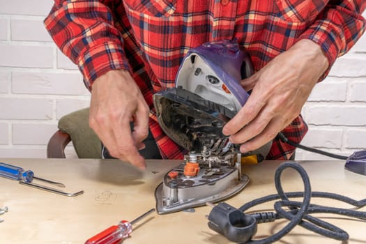 husband or the head of the family is trying to repair a broken steam iron at home on the table using simple tools. Disassembled electric iron. repairman checking and fixing broken iron