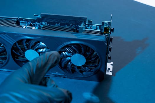 the hand of a computer technician holds a modern powerful video game card for a computer with three fans. the concept of PC hardware. Gaming video card with neon backlight