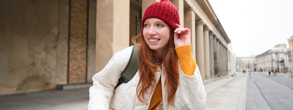 Young smiling redhead girl, student rides electric scooter, rents it and travels around city. Transport and travelling concept