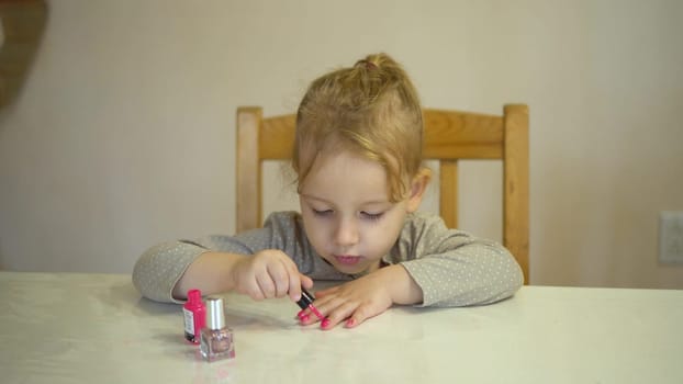 A little girl paints her nails with pink polish. The girl paints her nails like an adult. 4k