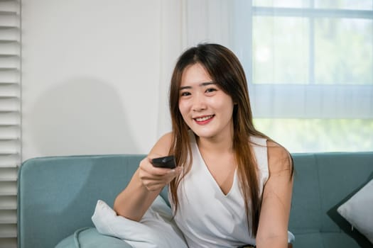 Happy female fun comedy video holding remote watching television, Asian young woman smiling sitting relaxing watch TV holding remote control on sofa in living room, Activity lifestyles concept