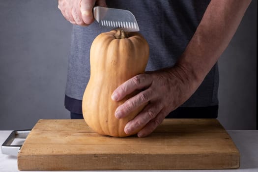 Caucasian unrecognizable middle-aged man cutting pumpkin on a wooden cutting board. Selective focus.