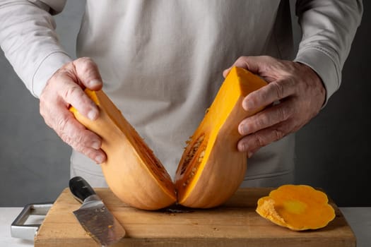 Caucasian unrecognizable middle-aged man cutting pumpkin on a wooden cutting board. Selective focus.