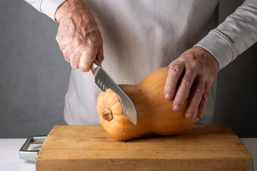 Caucasian unrecognizable middle-aged man cutting pumpkin on a wooden cutting board. Selective focus.