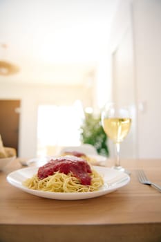 Still life with Italian spaghetti with fresh tomato sauce and a wineglass with white wine on the wooden table. Healthy eating. Nourishment. Italian food and traditions.