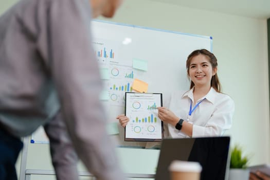 portrait of young asian business team presents business profits to colleagues at meeting, explaining business turn over on flipchart to coworkers in office with using tablet