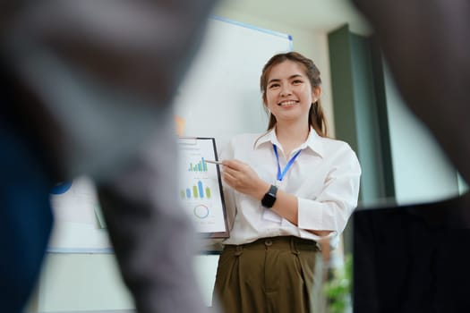 portrait of young asian business team presents business profits to colleagues at meeting, explaining business turn over on flipchart to coworkers in office with using tablet