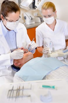 Female dentist and nurse doing operation on male patient