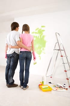 Rear view of embracing couple looking at wall with green paint on