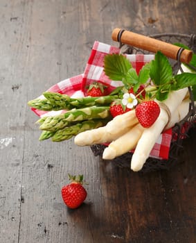 Green and white Asparagus and Strawberries in a wire basket on wooden background