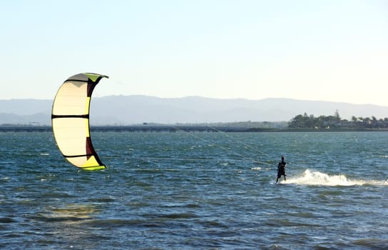 Kite surfer speeding across the water at sunset.