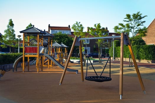 Public playground with colorful wooden climbing construction, swing, slides and rubber floor for safe playing