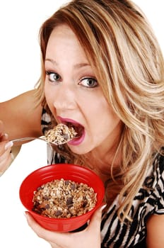 A very hungry young woman eating her breakfast from a red bowl, standing for white background, no time to sit down.