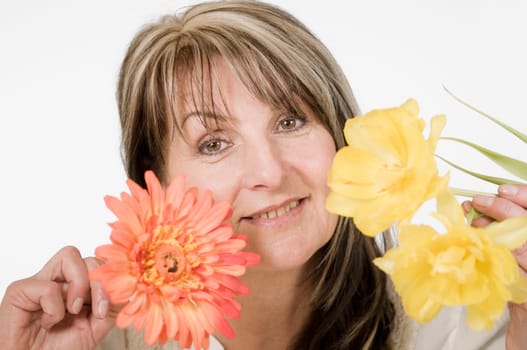 Head and shoulders portrait of middle-aged woman posing with orange-colored flower against neutral bright studio background