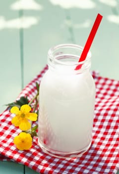 Glass milk bottle with red spoon in it, on checkered tablecloth