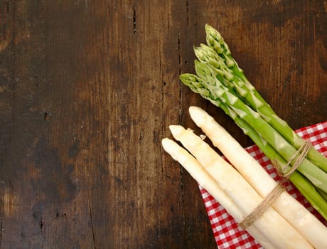 Fresh bunches of green and white asparagus lying on a checked napkin on a textured wooden surface with copyspace