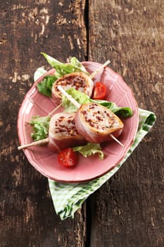 German Cuisine served on a vintage pink plate. Medallions of pork wrapped in bacon on an old wooden background. High angle view.