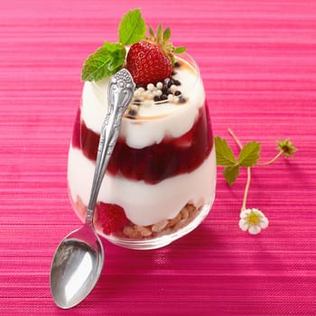Individual serving of a gourmet strawberry dessert with layered cream alternating with fresh fruit and purée in a glass container
