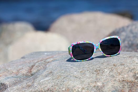 Sunglasses with colorful frame lying on a rock on the beach
