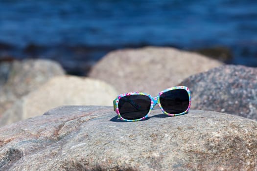 Sunglasses with colorful frame lying on a rock on the beach