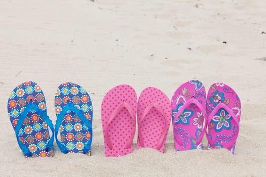 Three pairs of flip-flops on the sandy beach