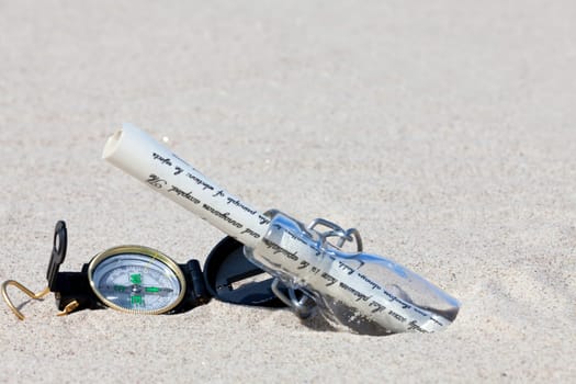 Message in a bottle with letter and compass in the sand