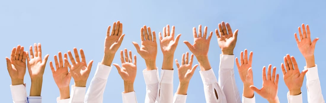 Close-up of several human hands raised against cloudy sky
