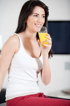 Young woman sitting on counter drinking orange juice