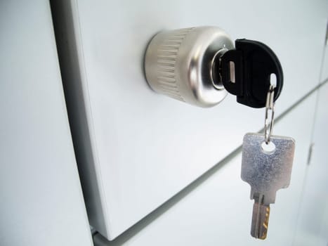 Close-up of a gray cabinet door with a round handle and inserted and hanging keys,as well as intersecting spacer gaps in oblique view